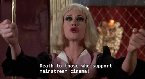 Cena do filme Cecil Bem Demente, onde a personagem principal Honey está de braços abertos e punhos cerrados dizendo “Morte àqueles que apoiam o cinema mainstream” (tradução oficial)