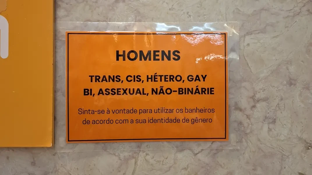 Cartaz inclusivo dos banheiros feminino e masculino, diz &ldquo;Trans, cis, hétero, gay, assexual, não-binárie, sinta-se à vontade para utilizar os banheiros de acordo com sua identidade de gênero&rdquo;