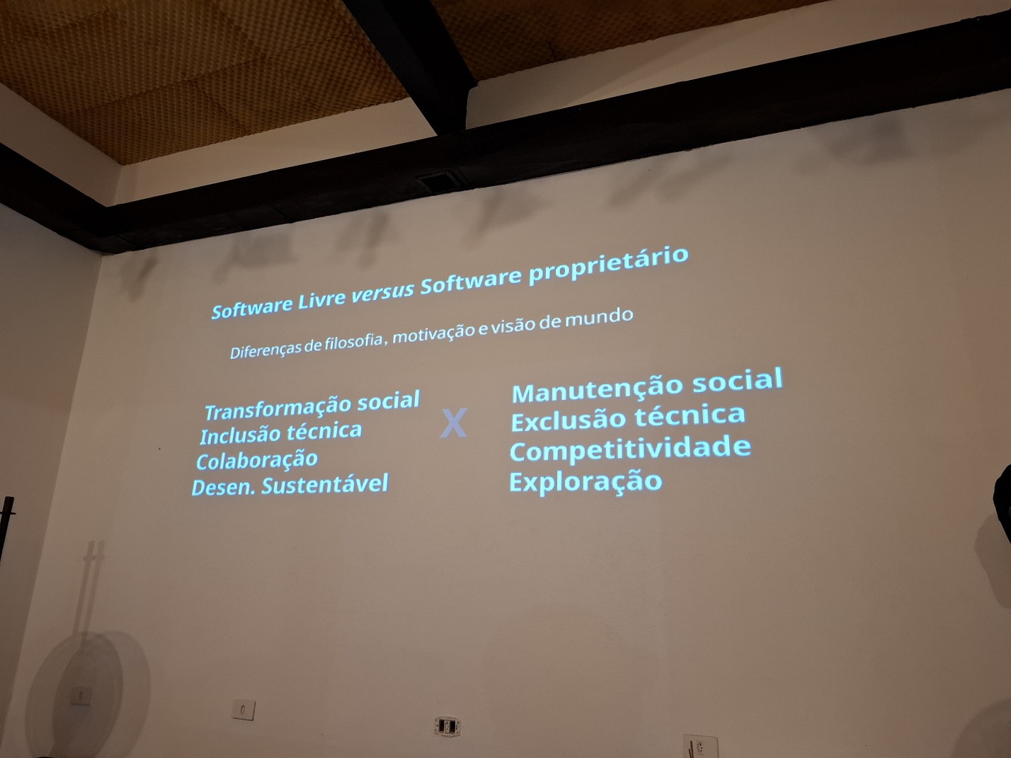 Um slide sendo projetado numa parede, com informações sobre a diferença entre software livre versus software proprietário
