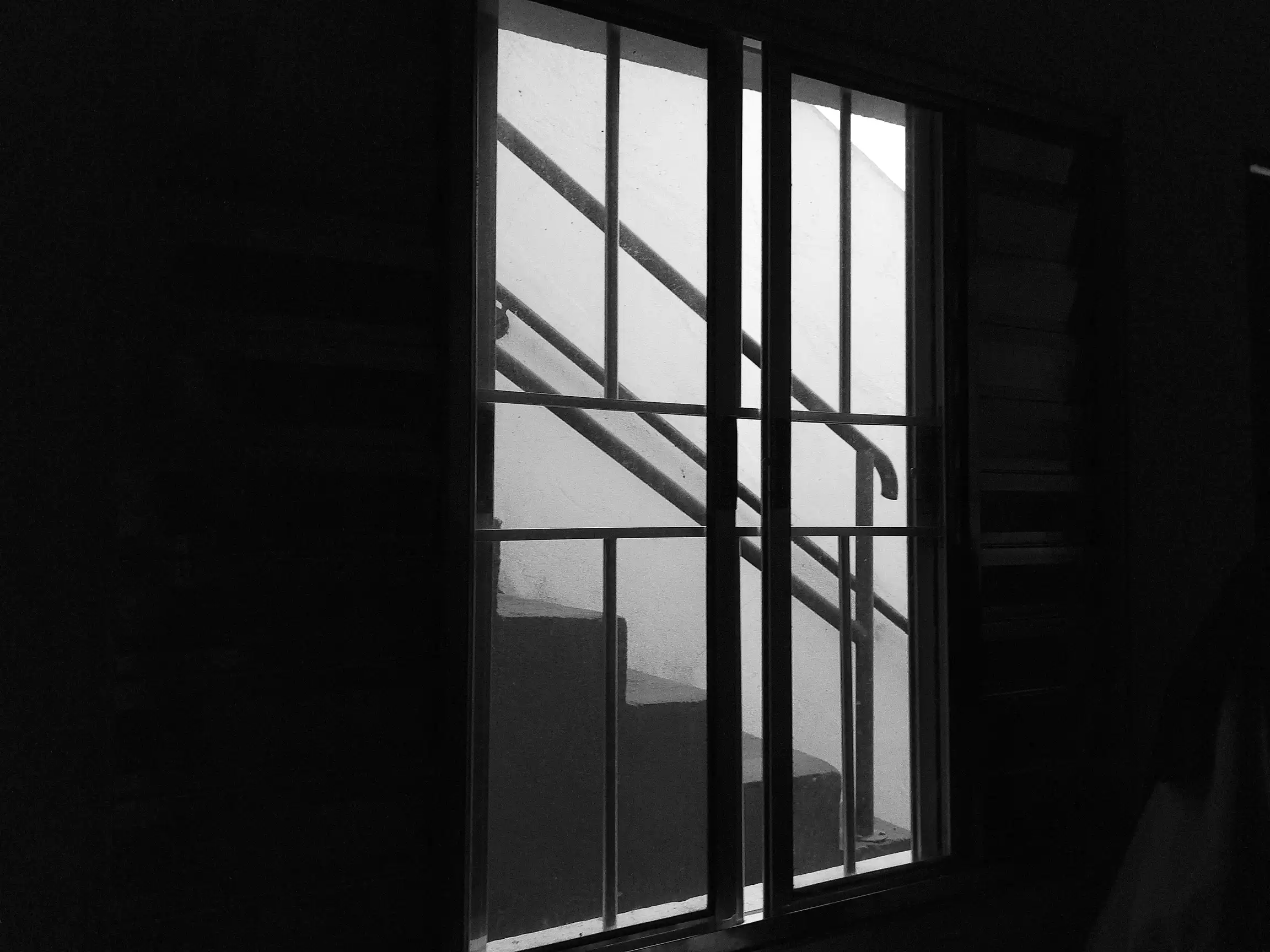Uma escada num dia chuvoso visto de dentro de um quarto, através de uma janela, preto e branco