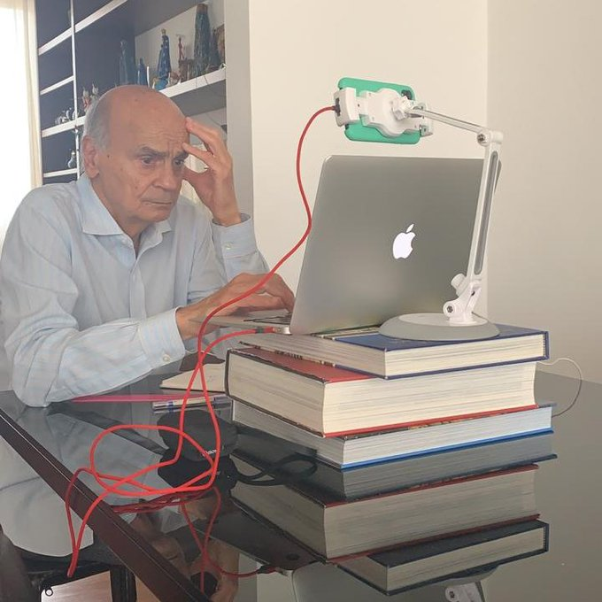 Drauzio Varella usando o computador em cima de uma pilhha de livros com uma cara pensativa